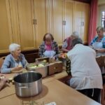 Več starejših žensk za mizo in pripravljajo sadje za nadaljno obdelavo.