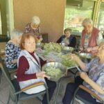 Skupina starejših žensk zunaj za mizo na kateri je bezeg.