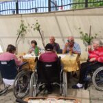 Skupina starejših ljudi sedi za mizo in je torto.