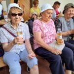 Tri starejše ženske sedijo na klopci in v rokah držijo plastenko vode.