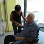 Ženska se rokuje s starejšim moškim, ki je na invalidskem vozičku.