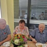 Trije starejši ljudje sedijo za mizo in jedo torto.