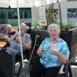 Več starejših žensk sedi na prostem in pije ledeno kavo.