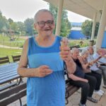 Starejši moški stoji, se smehlja in v rokah drži kornet s sladoledom.