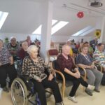Več starejših oseb sedi v notranjem prostoru.