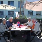 Štiri starejše osebe sedijo za mizo na prostem in zajtrkujejo.