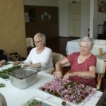 Tri starejše ženske sedijo za mizo in pripravljajo zelišča.
