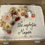 Fotografija torte, na kateri je napis "Vse najboljše Magda". Torta je okrašena z makroni, cvetovi iz sladkorne mase, figami, jagodami in rdečim ribezom.