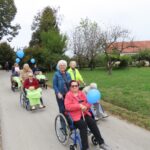 Stanovalci doma in prostovoljci so med sprehodom po poti na svežem zraku. Sprehajajo se skozi podeželsko pokrajino, obkroženi z naravo, s ciljem ozaveščanja in povezovanja ob "Sprehodu za spomin".